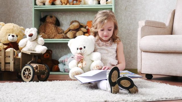 cute little girl reading a book with a teddy bear, play, have fun Funny lovely kid having fun in children room.