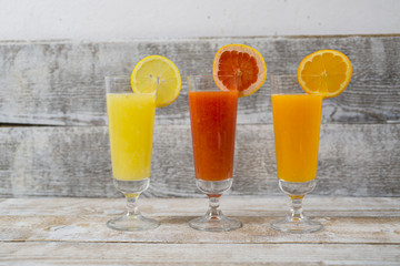 Citrus juices in glass and a slice of  lemon, grapefruit and  orange on wooden background .