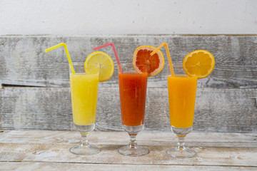 Citrus juices in glass and a slice of  lemon, grapefruit and  orange on wooden background .