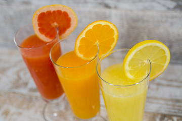 Citrus juices in glass and a slice of  lemon, grapefruit and  orange on wooden background .