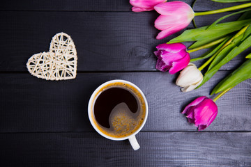Cup of coffee, wicker heart and bouquet of tulips on black wooden background