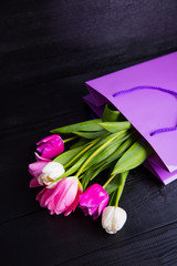 Bouquet of tender pink tulips in purple shopping bag on black wooden background
