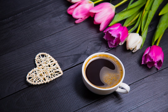 Cup of coffee, wicker heart and bouquet of tulips on black wooden background