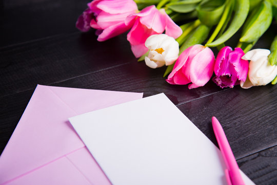 Bouquet of tender pink tulips and clear paper on black wooden background