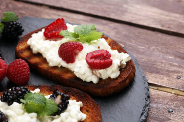 Bread with cheese cream and blackberries and raspberries for lunch table. Sharing antipasti on party or summer picnic time over wooden rustic background.