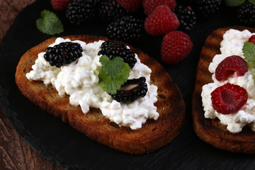 Bread with cheese cream and blackberries and raspberries for lunch table. Sharing antipasti on party or summer picnic time over wooden rustic background.