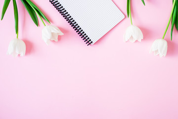 Floral's background. Tulips and notebook on pink background. Flat lay, top view. Woman day background.