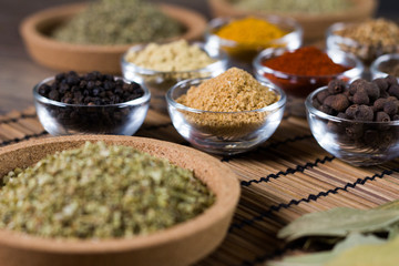 Various spices in bowls with fresh seasoning on rustic wooden background, closeup