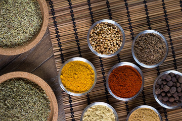 Various spices in bowls with fresh seasoning on rustic wooden background, closeup