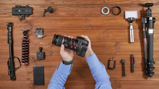 Male photographer takes a macro lens and extra ring from the camera. Wooden table top view. Equipment for shooting on the table