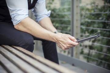 Man sitting on bench, using digital tablet, cropped