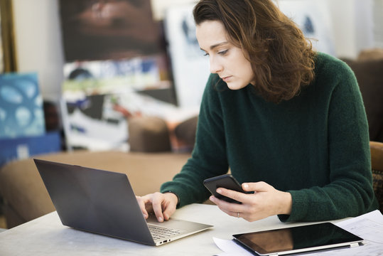 Woman multi-tasking with the help of laptop computer, digital tablet and smartphone