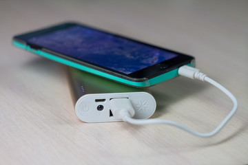 Phone is charging with energy bank on bright wooden background.