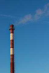 Steam escaping from pipe on the sky background at sunset, industrial emissions.