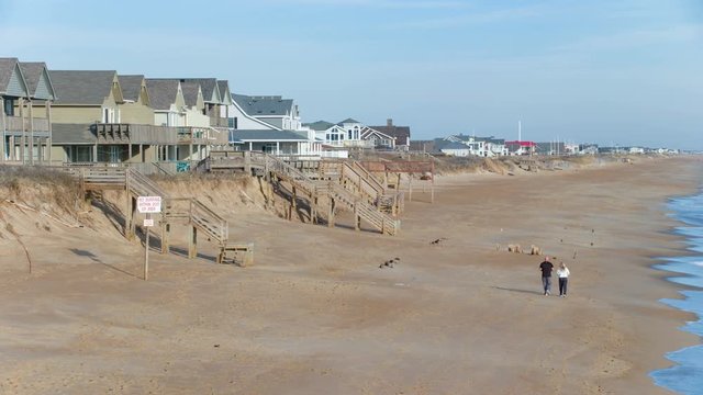 Couple Walking Along Outer Banks NC Beachfront with Beachfront Homes and Blue Atlantic Seawater on a Sunny Day in Kitty Hawk North Carolina