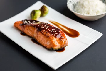  Teriyaki salmon on black background. Japanese cuisine inspired dinner consisting of grilled salmon fillet glazed in delicious teriyaki sauce (soy sauce base). Brussel sprouts and white rice as sides. © lounom