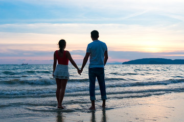 Young couple holding hands on the beach at spectacular sunset background
