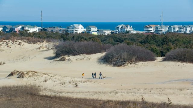 Jockey's Ridge State Park Visitors Walking with Dog on Sand Dune with Town of Nags Head NC Beachfront Building in the Background against the Blue Atlantic Ocean in North Carolina