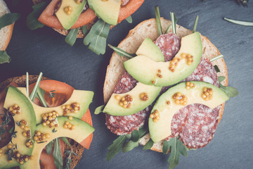 Sandwiches with salami, avocado and herbs on the black stone background. Toned image.