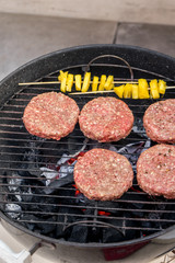 Grilled meat on a charcoal griddle accompanied by onions in foil and pineapple.