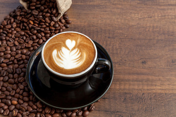 Coffee cup of latte art in the black color cup with some coffee beans on wooden background