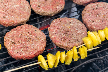 Grilled meat on a charcoal griddle accompanied by onions in foil and pineapple.