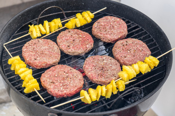 Grilled meat on a charcoal griddle accompanied by onions in foil and pineapple.