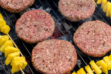 Grilled meat on a charcoal griddle accompanied by onions in foil and pineapple.