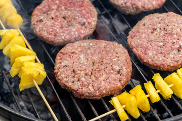 Grilled meat on a charcoal griddle accompanied by onions in foil and pineapple.