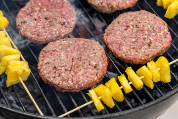 Grilled meat on a charcoal griddle accompanied by onions in foil and pineapple.