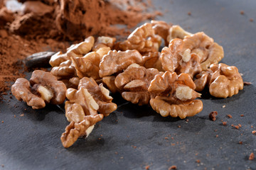 peeled walnuts kernels with cacao powder close-up  on black slate plate
