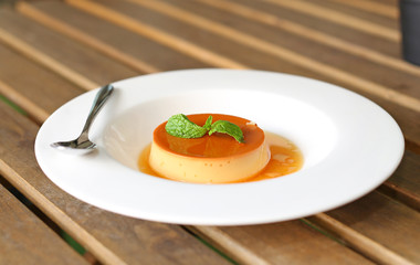Caramel custard cake with peppermint leaf in white plate on wooden table.