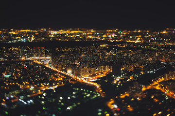 True tilt shift shooting of residential district of night metropolis from very high above: multiple residential houses and orange lights from windows, strong bokeh in background and foreground