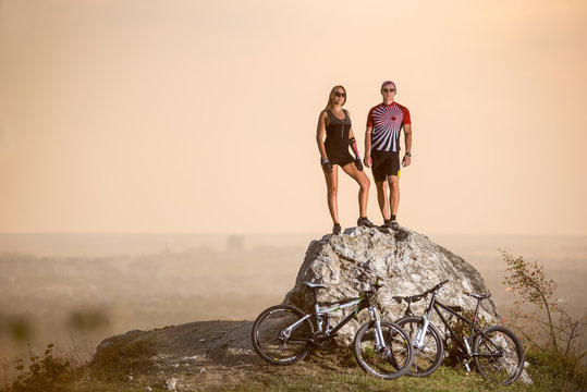 Summer evening. Cyclists standing on a large stone on the precipice of a cliff next to them are sports bikes. Blurred background with copy space