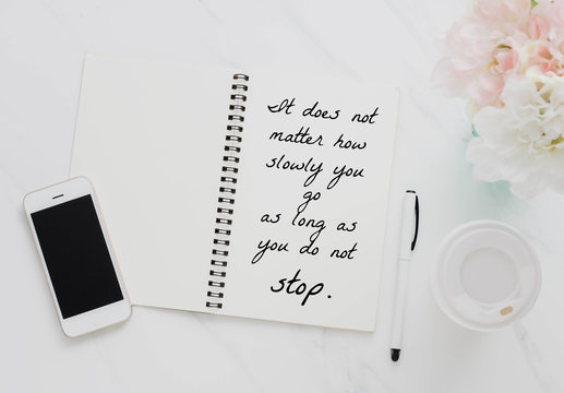 Inspirational motivating quote on notebook with smartphone, coffee cup and flower on white marble table background.