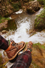 Vista en primera persona de alguien con botas de montaña en una excursión sentado sobre una cascada 