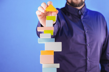 Businessman building tower of colorful wooden blocks. Concept of business success, achievement and...