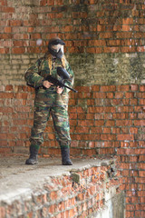 girl playing paintball in overalls with a gun.