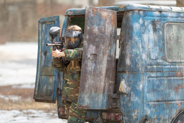 girl playing paintball in overalls with a gun.