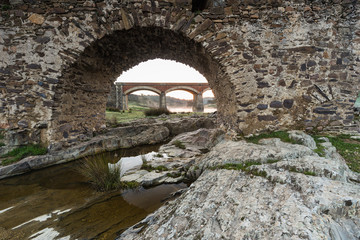 Fototapeta na wymiar Ancient Roman bridge over the Salor river, located near Aliseda. Extremadura. Spain. Across one of the eyes of the Roman bridge, a modern bridge is seen.