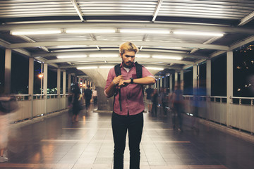 Handsome bearded man standing on the street while looking at smartwatch traveling at night.