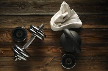 Top view of black iron kettlebell, dumbbell and white towel on wooden floor Sport background with copyspace