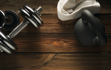 Top view of black iron kettlebell, dumbbell and white towel on wooden floor Sport background with copyspace