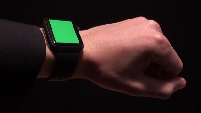 Businessman with smartwatch with green screen, chroma, black background. Man dressed in a dark jacket worn on the left wrist smartwatch. Adrian