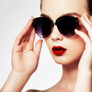 Fashion sunglasses. Sexy woman in swimsuit with golden sunglasses and fashion makeup. Glamour shot of a beautiful model with red lips. Young girl posing in white swimsuit a on white background