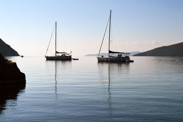 Early morning by the sea, silhouettes of two yachts in the calm water of the bay