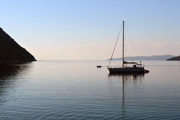 Early morning by the sea, silhouette of a single yacht in the calm water of the bay