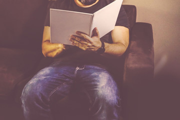 A person holding a white paper notebook sitting in a black coffee chair.