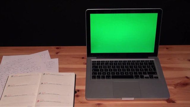 Laptop with green screen chroma on a wooden table and black background. Adrian