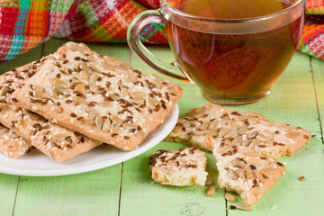 crispy bread with seeds of sunflower, flax and sesame seeds with a cup of tea on a green wooden background